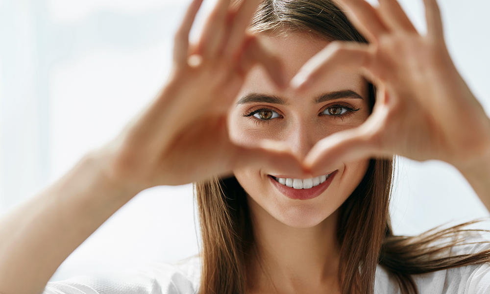 Healthy Eyes And Vision. Portrait Of Beautiful Happy Woman Holding Heart Shaped Hands Near Eyes. Closeup Of Smiling Girl With Healthy Skin Showing Love Sign. Eyecare. High Resolution Image